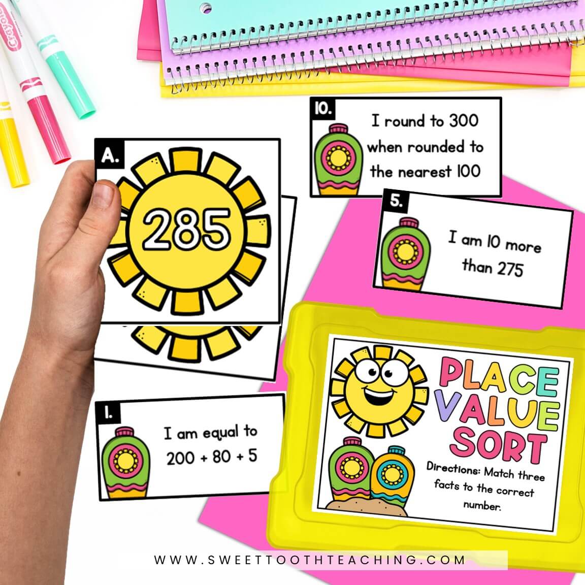 A student holds a place value card showing 285; math task cards, markers, notebooks, and a Place Value Sort kit for centers.